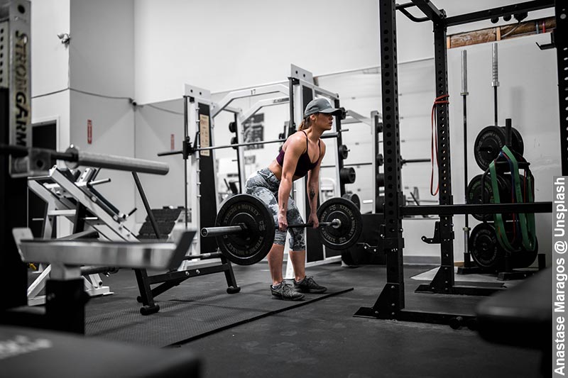 A woman performing an Isometric Deadlift Hold in a gym environment, symbolising the practice of Lowering High Blood Pressure with Isometric Resistance Training.