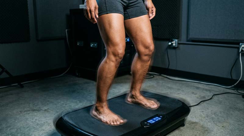 The lower body of an adult stands barefoot with slightly bent knees as subtle movement passes through the vibrating platform.