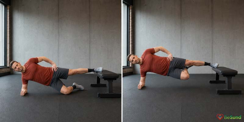 A man of average build lifts his bent lower leg towards his supported upper thigh while holding a side plank beside a gym bench.