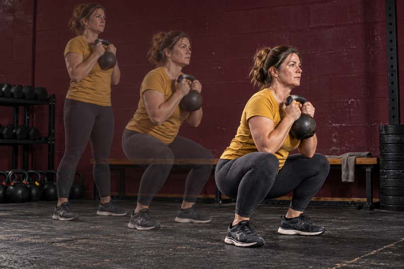 Multiple exposures show a woman in a yellow T-shirt lowering into a goblet squat with a kettlebell.