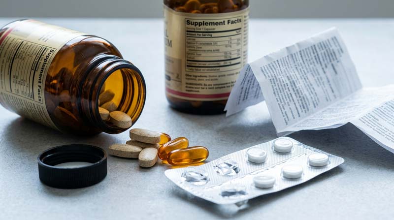 Supplements spilling beside a prescription blister strip illustrate potential interactions when taking too many supplements.