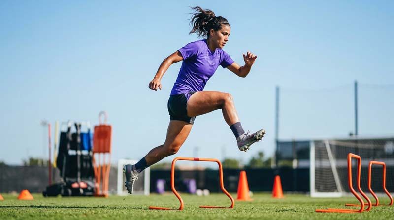 A footballer leaps over an orange training hurdle, illustrating tendon loading explored in collagen peptides research.